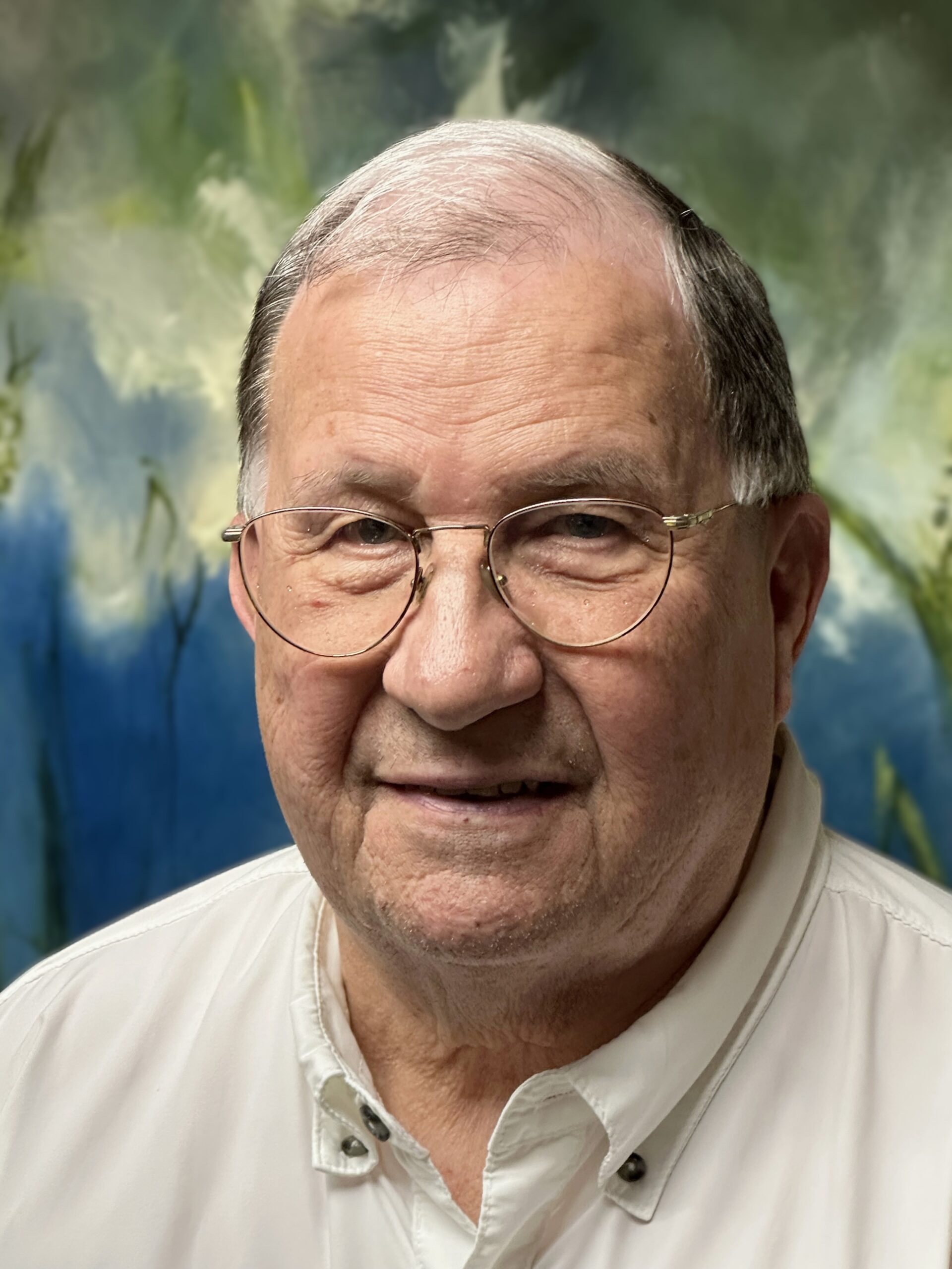 Photograph of a man with wire-frame glasses wearing an off-white open-collared shirt.